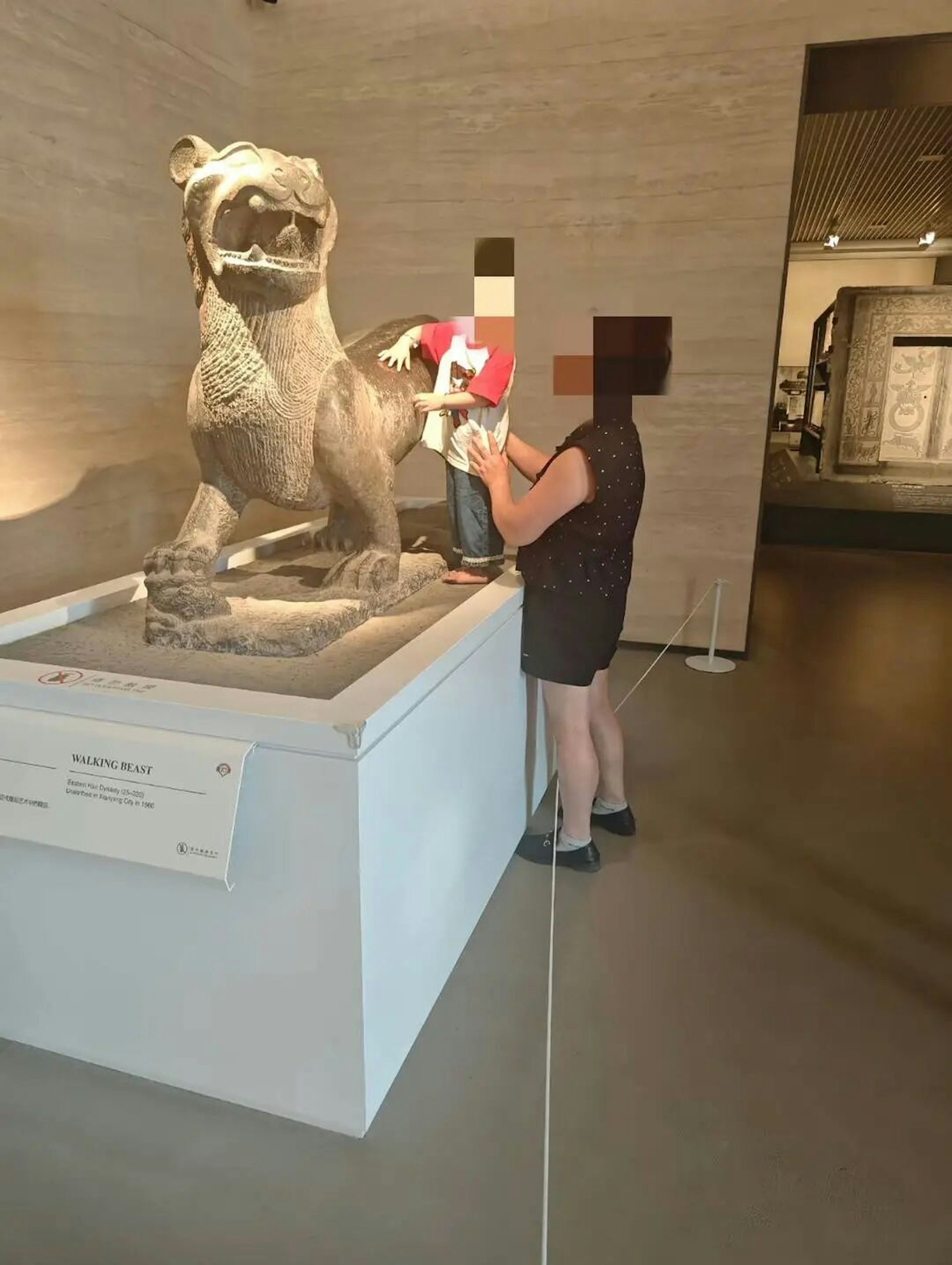 網上圖片顯示，在西安碑林博物館展廳內，有一名男童赤腳站在展台上，雙手觸摸東漢石走獸，一名年長女士則從旁用雙手扶著男童。（網上圖片）