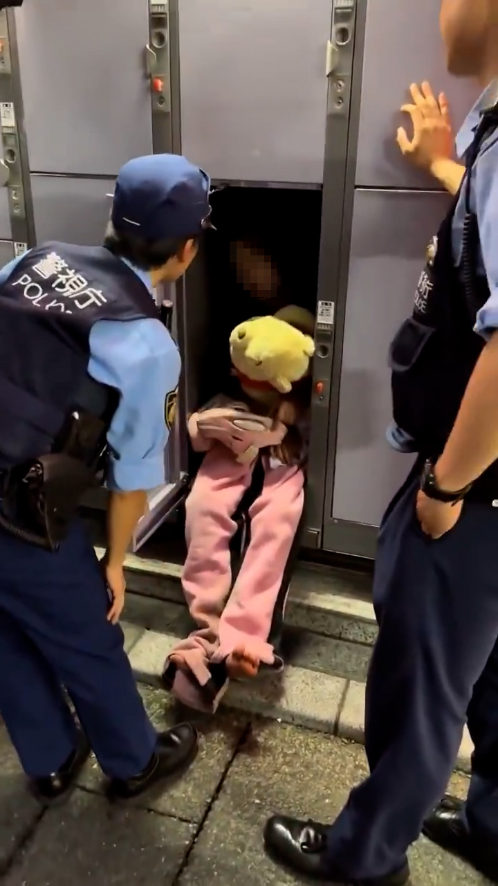 一名身穿睡衣的年輕女子，抱著毛公仔，坐在街上的儲物櫃裏，有警員把她喚醒。（「X」影片截圖／alex001050）