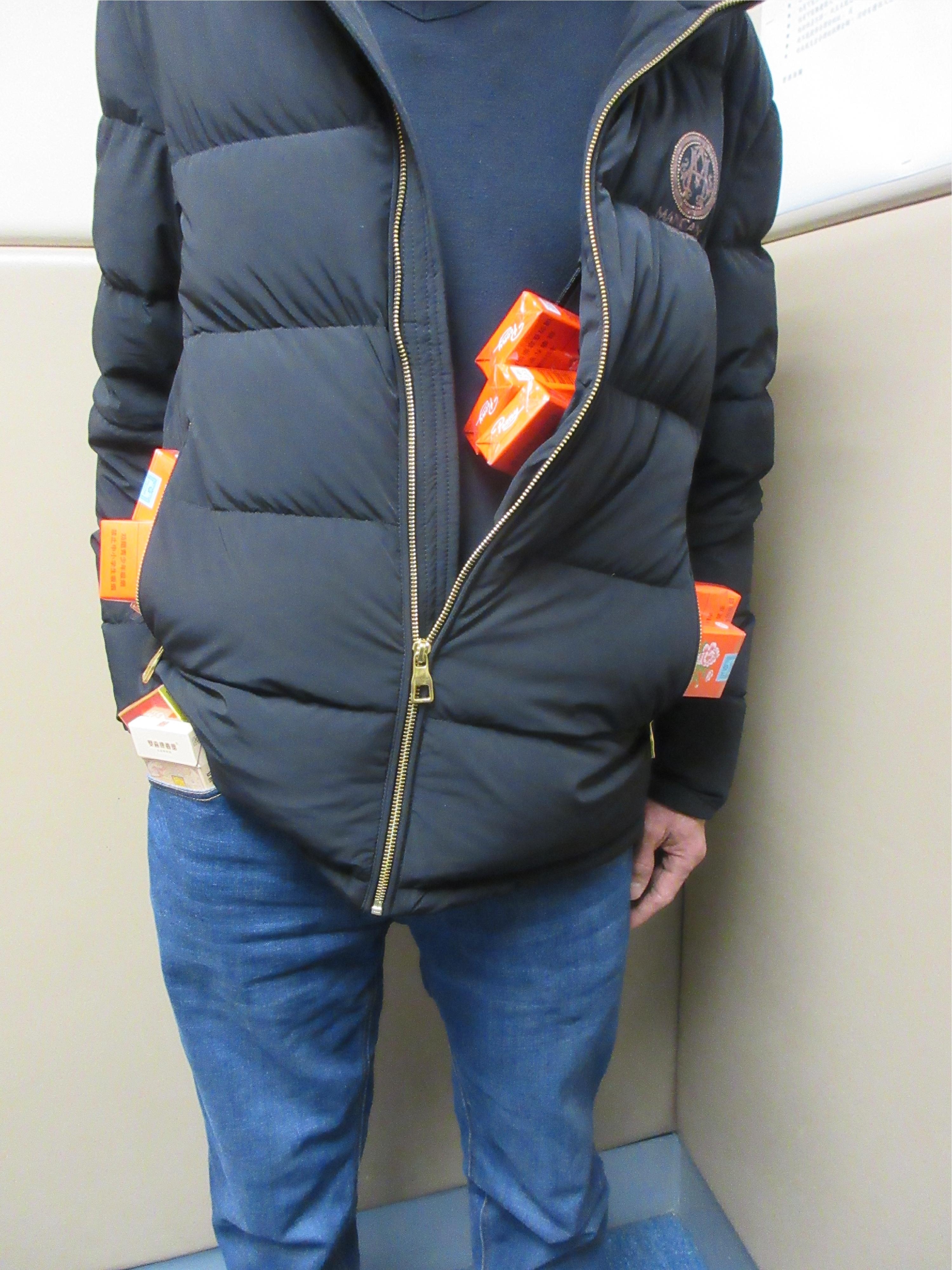 圖示該名旅客在外套袋及褲袋內收藏未完稅香煙。（海關圖片）