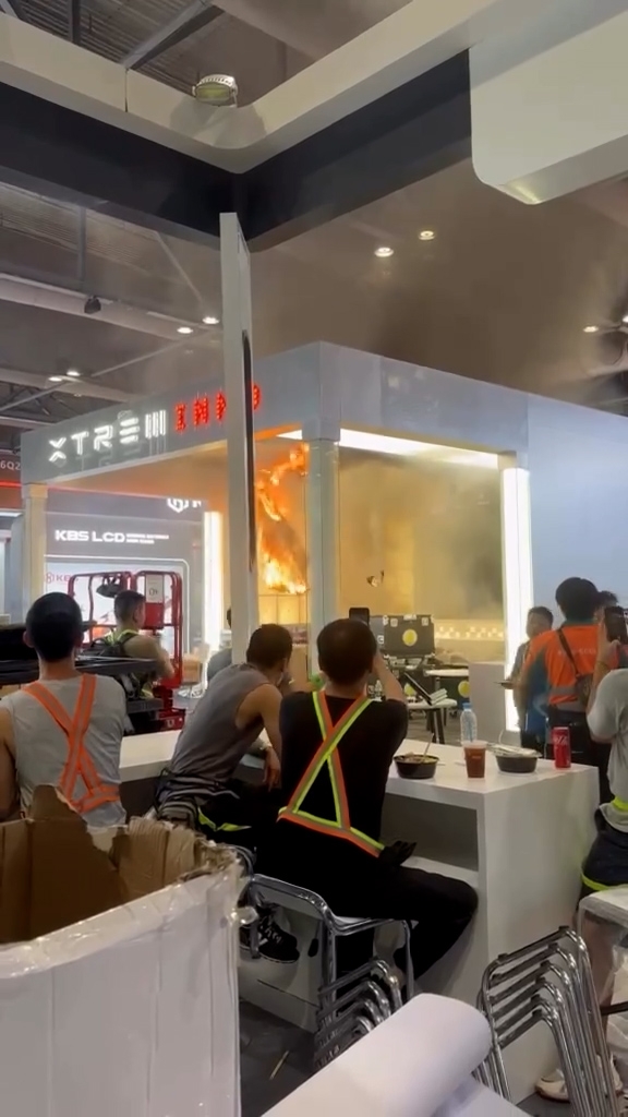 火勢主要集中在攤位的天花位置，火焰和濃煙不斷冒出，有著火的物料掉落，現場有不少工人圍觀。（Threads影片截圖／@markkwok_____）