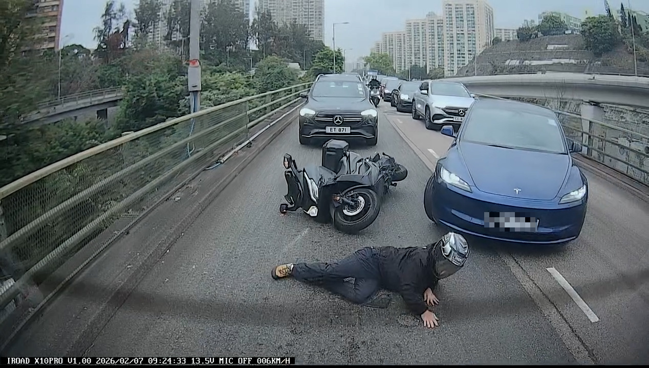 一輛電單車「攝車隙」在兩線中間駛至，此時左邊行車線一輛深藍色Tesla私家車突然向右扭軚切線，電單車鐵騎士閃避不及，撞上Tesla私家車發生碰撞，人車翻倒跌在地上。（Facebook影片截圖／車cam L（香港群組）／KM Pang）