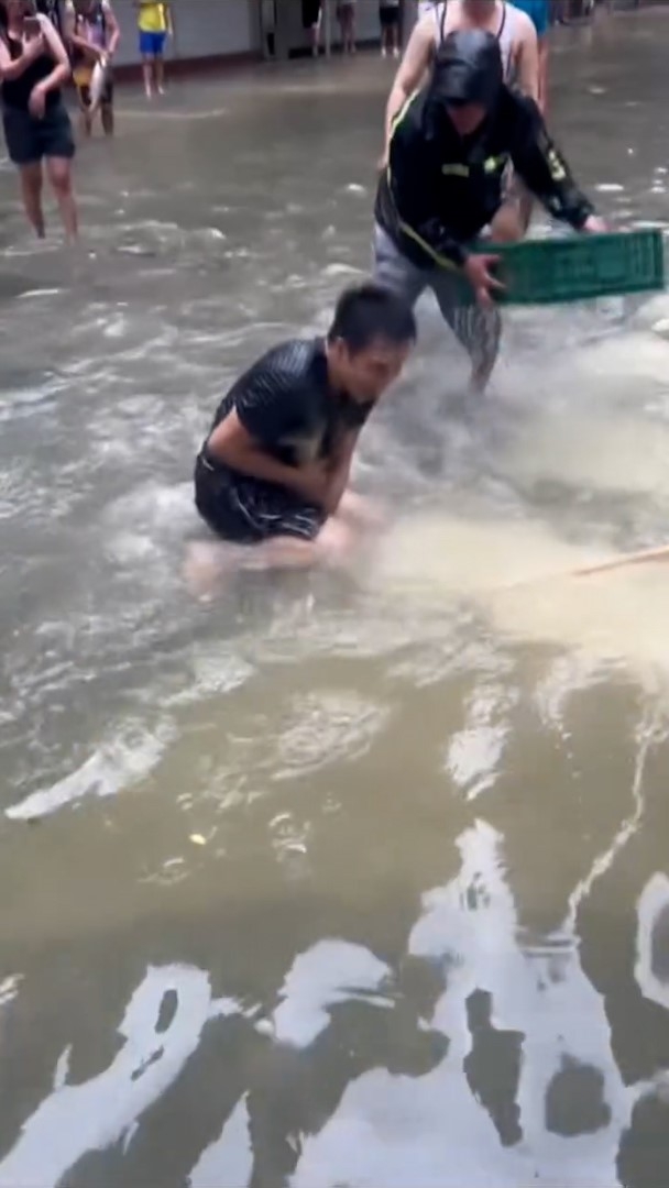 大批民眾聚集在被水淹蓋的街道上，興高采烈地捉魚，場面熱鬧，最終有人成功將活蹦亂跳的魚捉起。（Facebook影片截圖／澳門Secret）