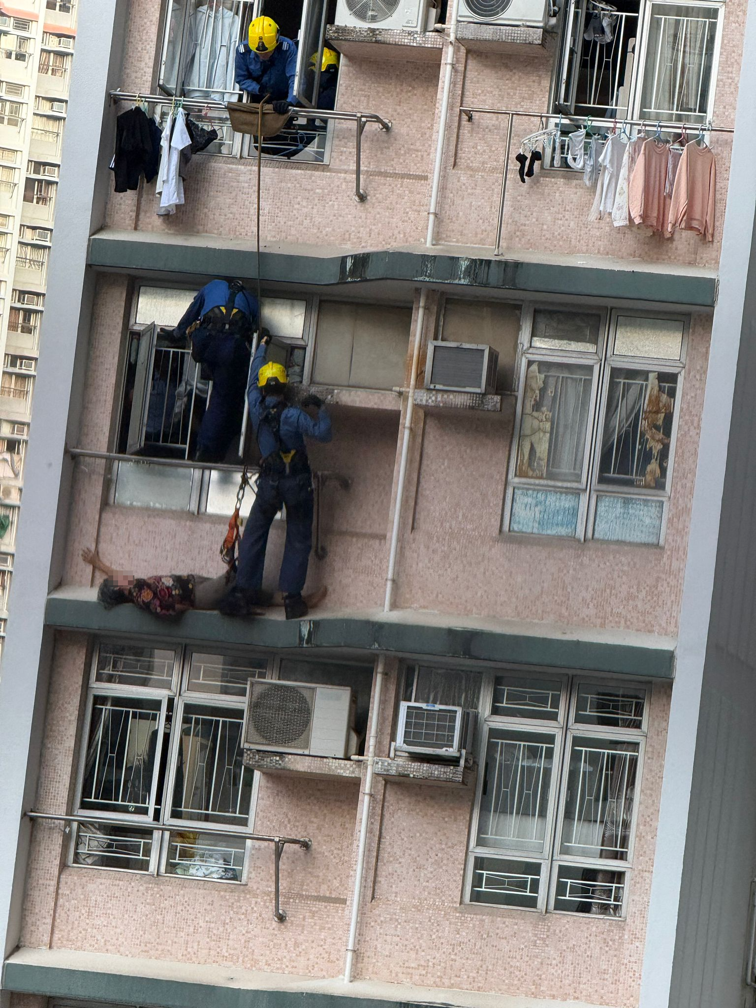數名消防員游繩至事發單位外，經窗戶將老婦救回單位內，單位內亦有警員協助，過程歷時大約1至2分鐘。（報料觀眾提供相片）