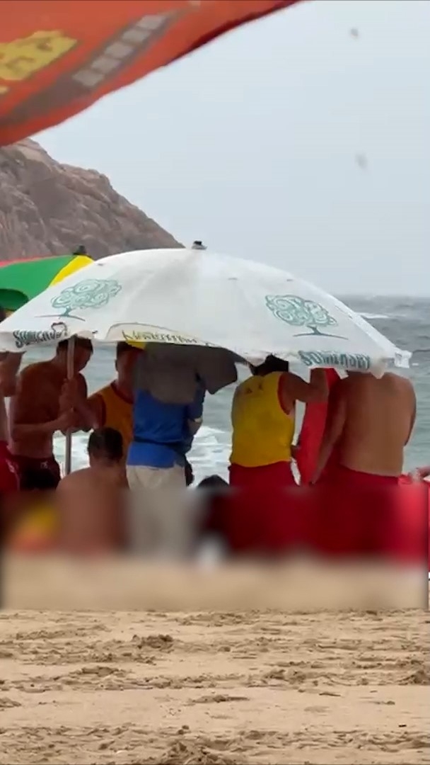 現場下起大雨，有泳灘職員和救生員撐起太陽傘遮擋。（觀眾提供影片截圖）