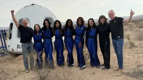 Dave Limp/Blue Origin 一群九人站在沙漠景觀中的藍色起源新謝潑德太空艙前。六名 NS-31 女性機組人員穿著統一的藍色飛行服。從左到右：傑夫·貝佐斯、凱里安·弗林、凱蒂·佩里、勞倫·桑切斯、艾莎·鮑、蓋爾·金、阿曼達·阮、奧黛麗·鮑爾斯和戴夫·林普。亞軌道飛行成功後，大家合影留念，心情十分愉悅。