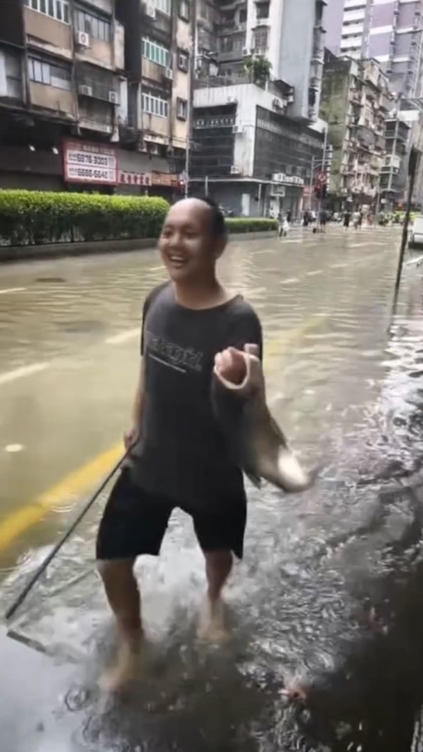 大批民眾聚集在被水淹蓋的街道上，興高采烈地捉魚，場面熱鬧，最終有人成功將活蹦亂跳的魚捉起。（Facebook影片截圖／澳門Secret）