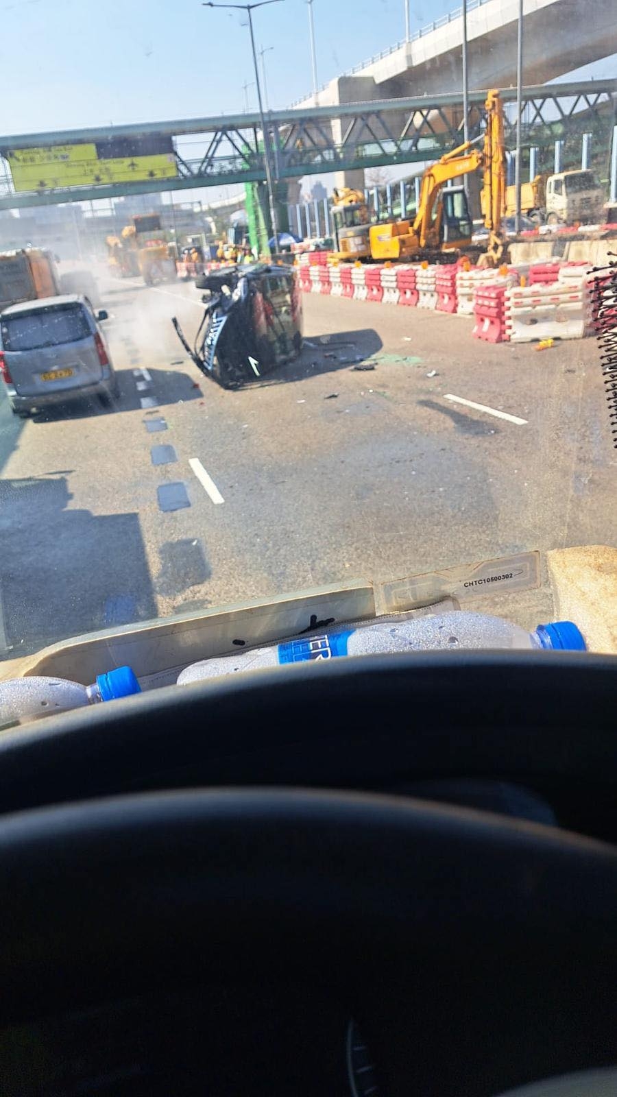 涉事黑色私家車向左翻側，橫亘路中，車尾冒白煙，車頭嚴重損毀，零件碎片散落一地。（Facebook圖片／車cam L（香港群組）／Bosco Chu）