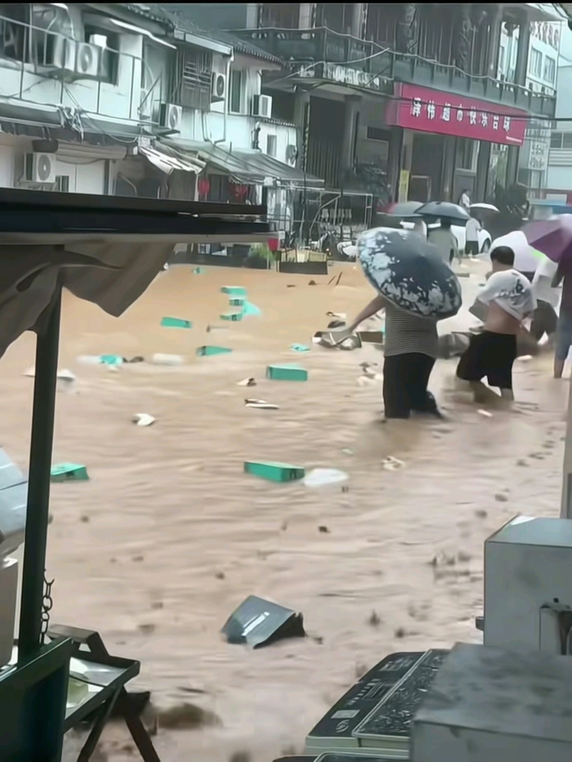 在浑浊的积水中，大量鞋盒和各式鞋子随水漂流，不少民众撑著雨伞在街边捡拾被水冲出来的鞋子。（网上影片截图）