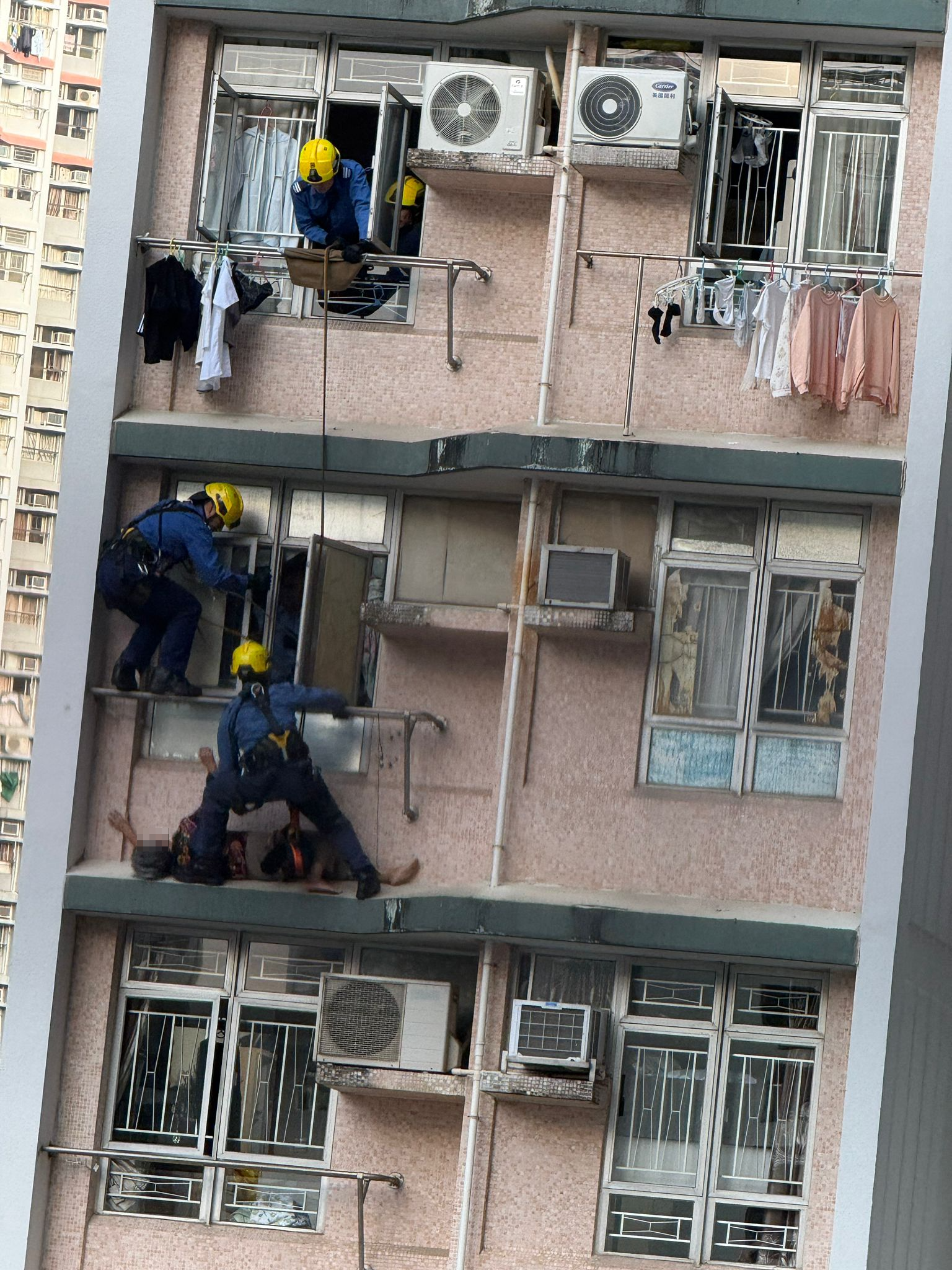 數名消防員游繩至事發單位外，經窗戶將老婦救回單位內，單位內亦有警員協助，過程歷時大約1至2分鐘。（報料觀眾提供相片）