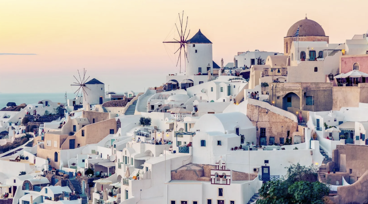 聖托里尼日落時分，白色洞穴屋與經典風車在橙色天空下，呈現希臘群島通行證的浪漫島嶼體驗。