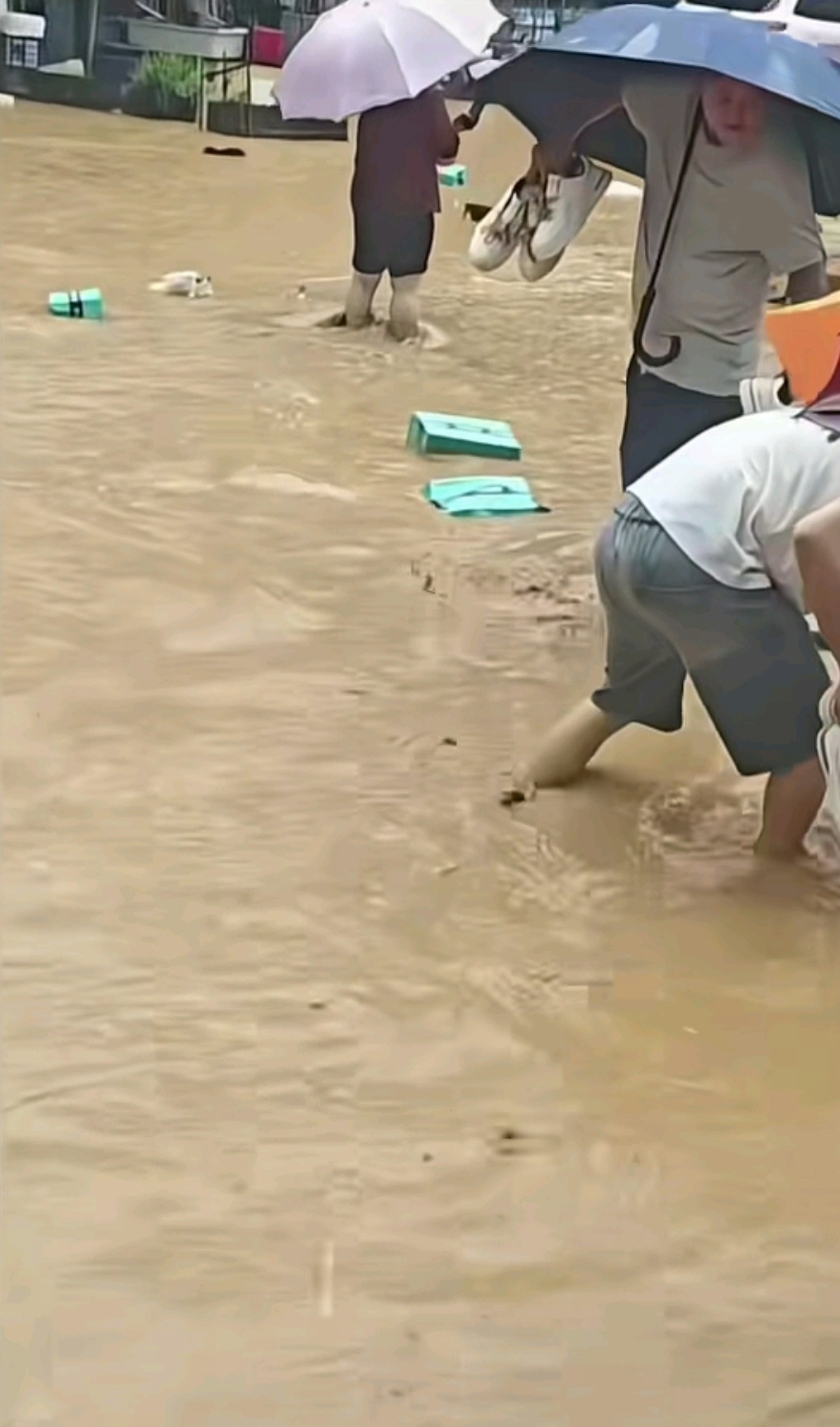 在浑浊的积水中，大量鞋盒和各式鞋子随水漂流，不少民众撑著雨伞在街边捡拾被水冲出来的鞋子。（网上影片截图）