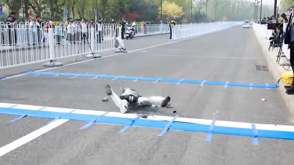 涉事機械人被一條藍白相間的起跑線絆倒，隨後摔倒在地，手臂部位瞬間脫離飛開，不少零件散落一地。（網上影片截圖）