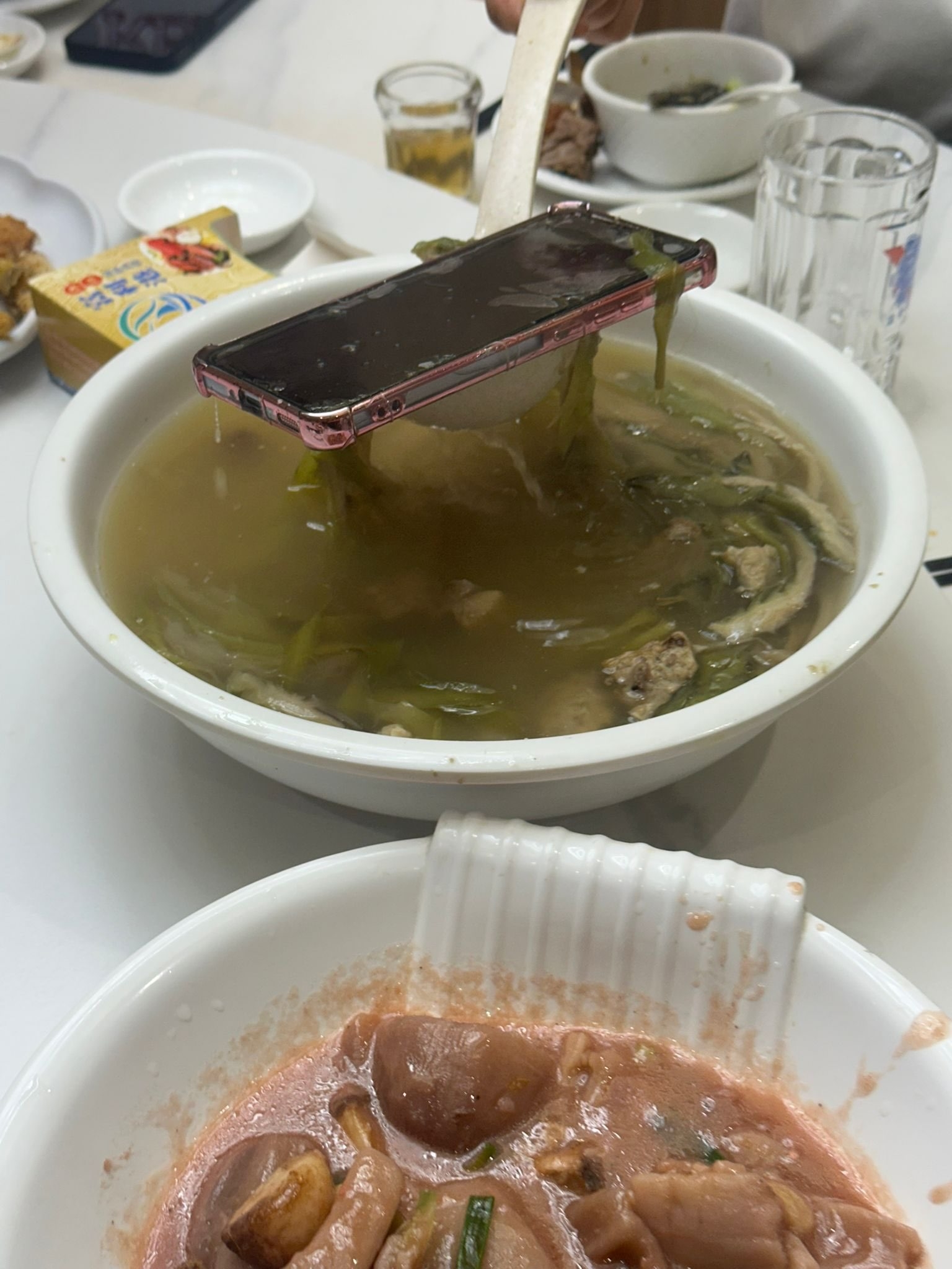 在餐桌上，有人用湯勺撈起一部手機，而手機上還沾著數片菜葉。（Threads圖片／@hyunnisgood）