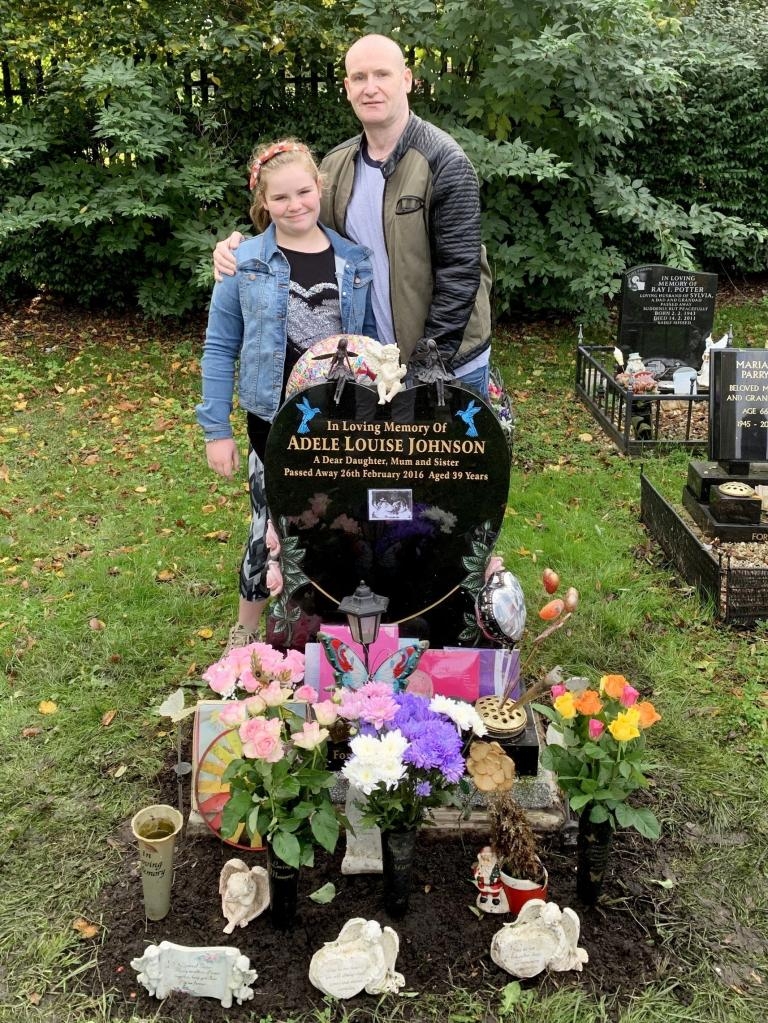 John Granahan and his daughter Olivia standing next to a heart-shaped grave marker for Adele Louise Johnson.