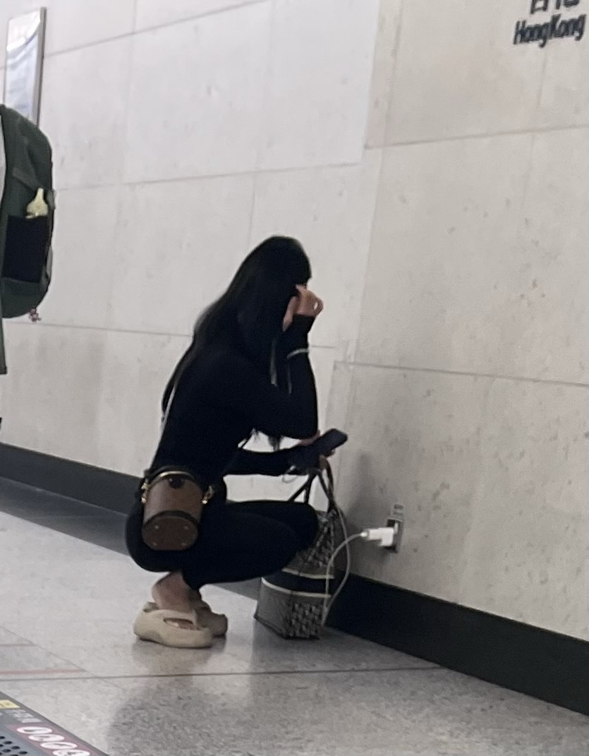 現場為港鐵香港站，1名隨身帶著疑似名牌斜揹袋及手提袋的長髮女子蹲在地上，將自攜的充電線及插蘇，插入牆身低處的插座，疑是在為自己的手機充電。（Threads圖片／local_delulu_hooman）