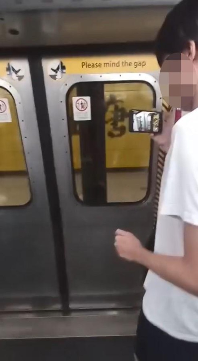 擋門的白衣男子手上拿着手機拍攝。（網上片段截圖）