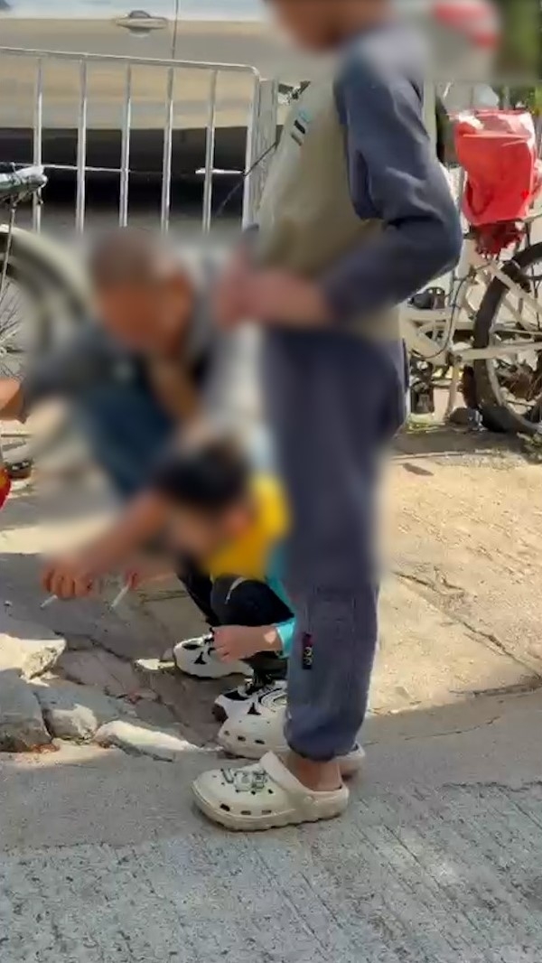 涉事小朋友和男性長輩一同蹲在街上吸煙，較年長的小朋友則站在旁邊。（報料觀眾提供影片截圖）