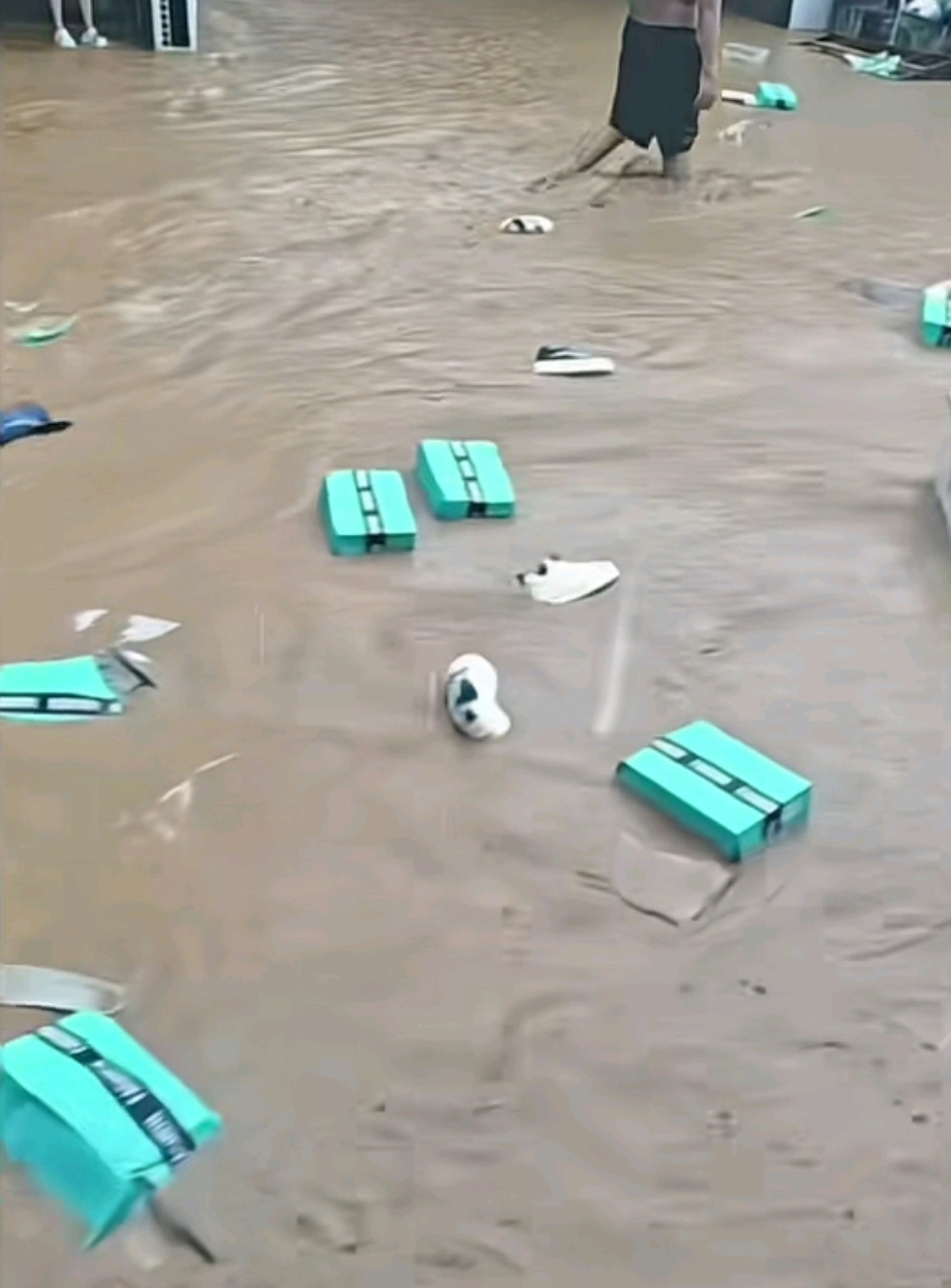 在浑浊的积水中，大量鞋盒和各式鞋子随水漂流，不少民众撑著雨伞在街边捡拾被水冲出来的鞋子。（网上影片截图）