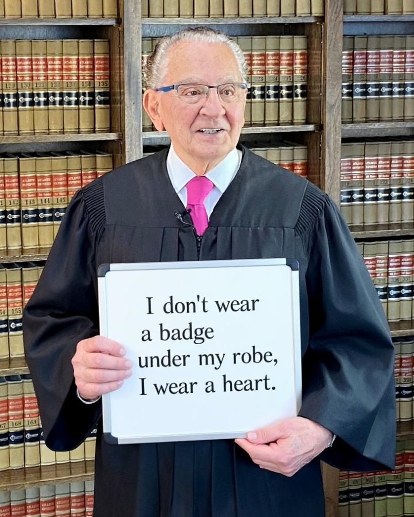 法官弗蘭克·卡普里奧舉著一塊牌子，上面寫著：“我的長袍下沒有佩戴徽章，我戴著一顆心。”