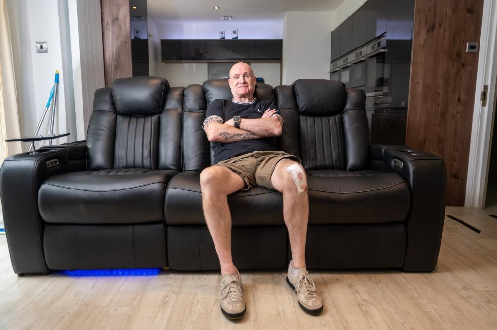 A man with a bandage on his knee sitting on a black leather sofa.