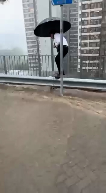 打工仔暴雨下在山崖邊的防撞欄上行走。