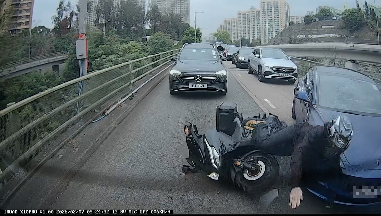 一輛電單車「攝車隙」在兩線中間駛至，此時左邊行車線一輛深藍色Tesla私家車突然向右扭軚切線，電單車鐵騎士閃避不及，撞上Tesla私家車發生碰撞，人車翻倒跌在地上。（Facebook影片截圖／車cam L（香港群組）／KM Pang）