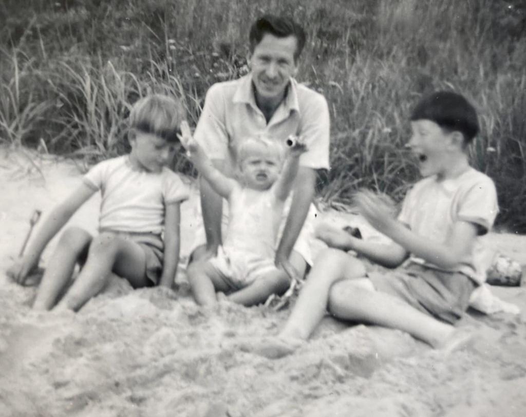 一名男子和三個孩子在沙灘上玩耍的黑白照片。